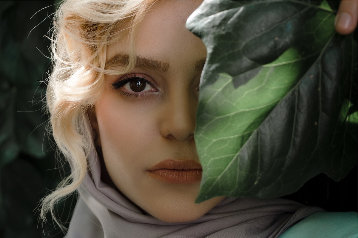 girl in white hijab covering her face with green leaves